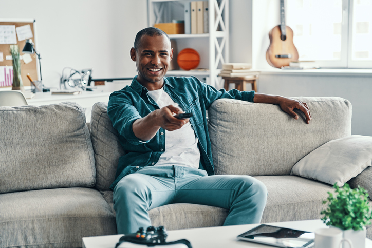 Handsome young African man holding television set and smiling while sitting indoors