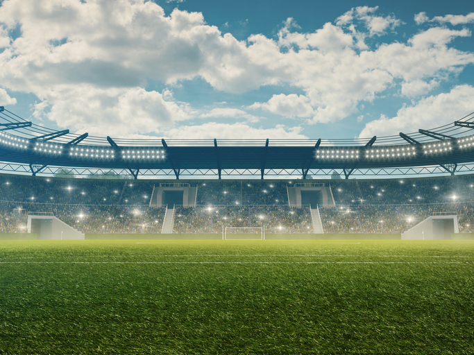 Soccer stadium with tribunes, illumination, green grass and cloudy blue sky